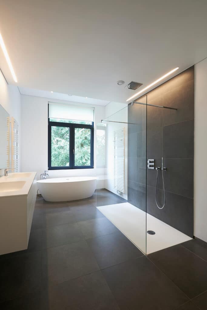 Salle de Bain Design: Douche Verre & Baignoire Moderne Salle de bain moderne avec grande douche carrelée gris foncé, baignoire îlot blanche, double vasque et fenêtre sur la verdure.