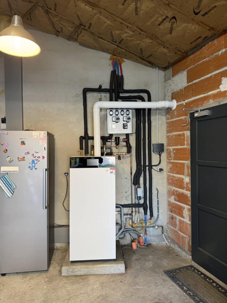 Installation Viessmann de chauffage moderne avec tuyauterie isolée noire, panneau de contrôle et manomètres, dans un local technique brut. Isolation Thermolan au plafond.